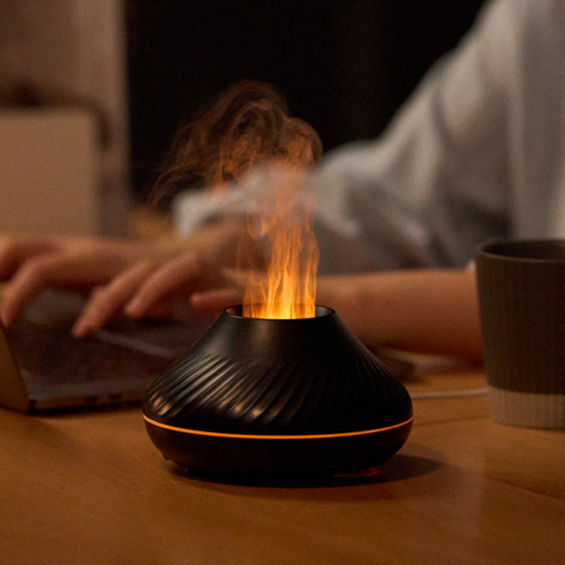 Black flame diffuser glowing orange on a desk next to a laptop